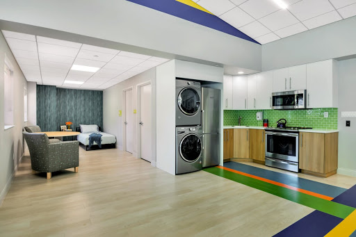 A modern apartment interior featuring a laundry unit, kitchen area, and living space with colorful accents.