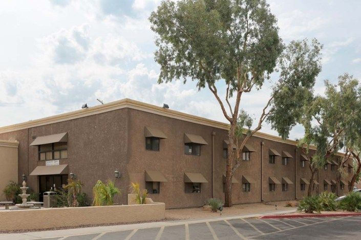 A residential apartment building with trees in front and a cloudy sky backdrop.
