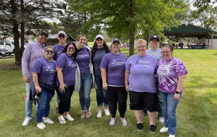 A group of people wearing purple shirts gathered outdoors in a park setting.