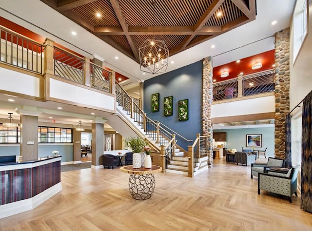 A modern and spacious hotel lobby featuring a stylish chandelier, elegant wooden flooring, and a grand staircase.