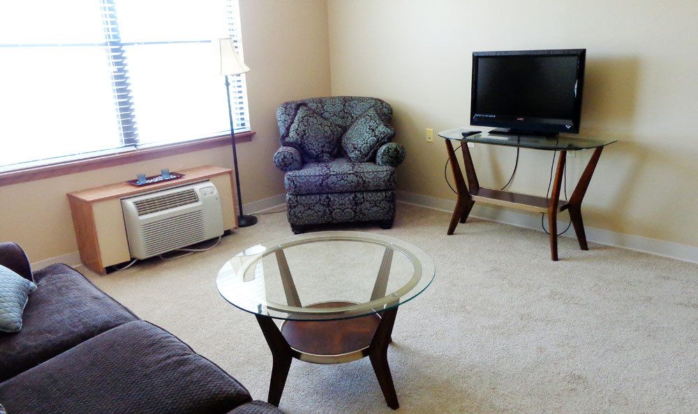 A cozy living room with a chair, glass coffee table, and TV.