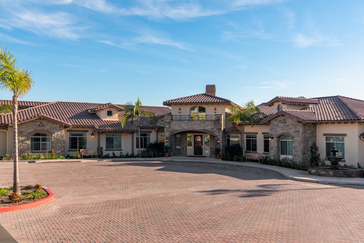 A large, luxurious mansion with a paved driveway under a clear blue sky.