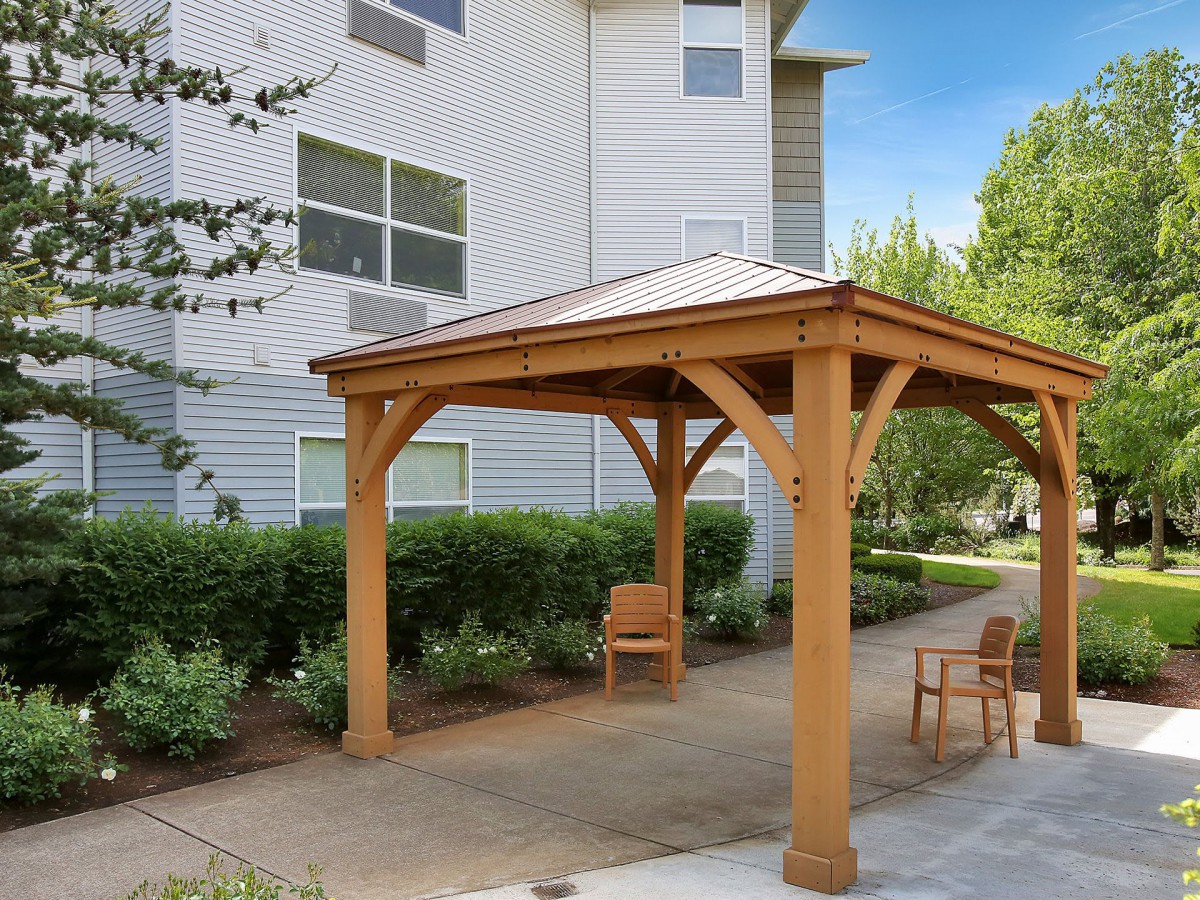 A wooden gazebo with outdoor chairs in a garden patio area.