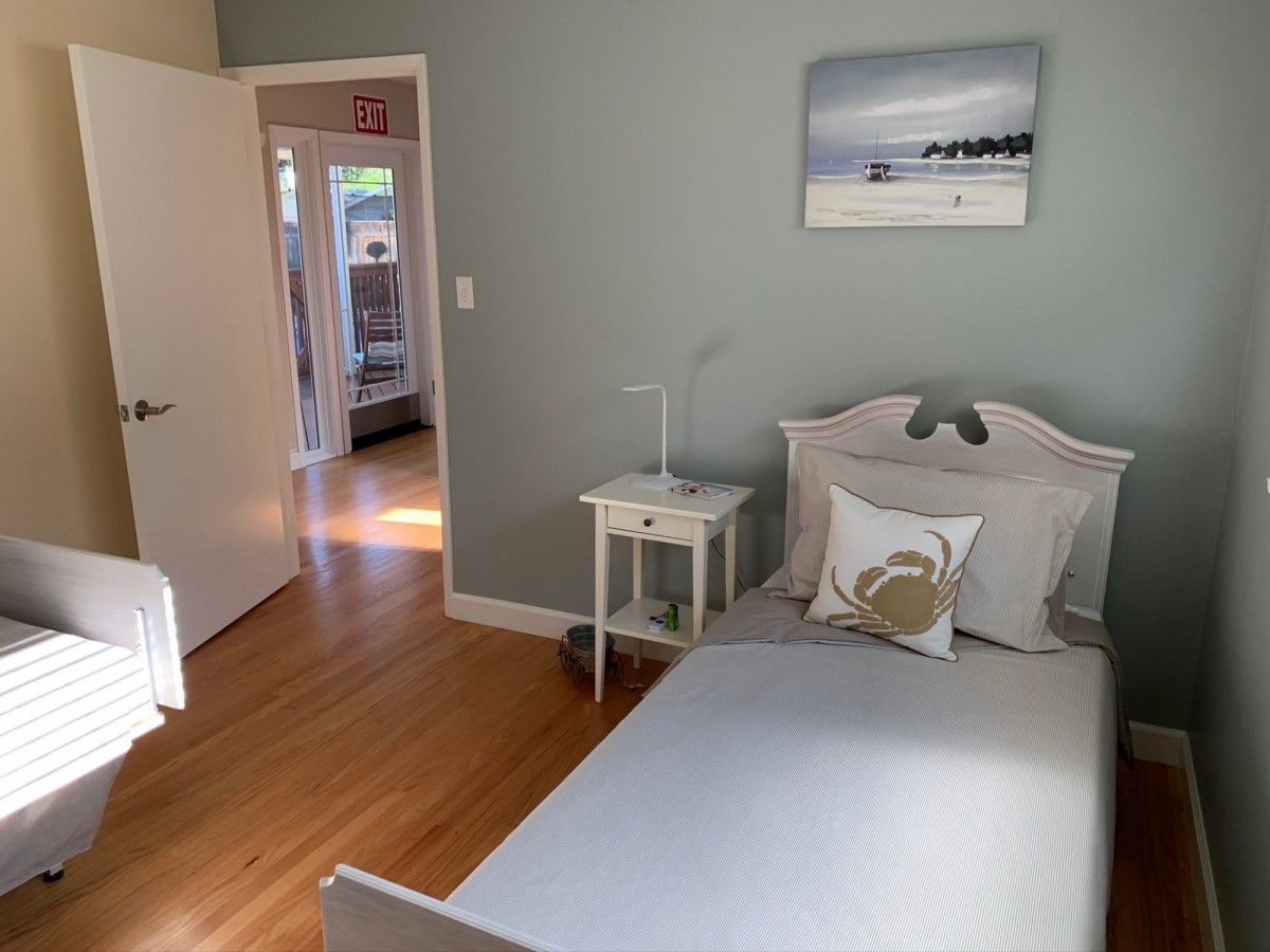 A cozy bedroom featuring a neatly made bed, a nightstand, and soft wooden flooring.