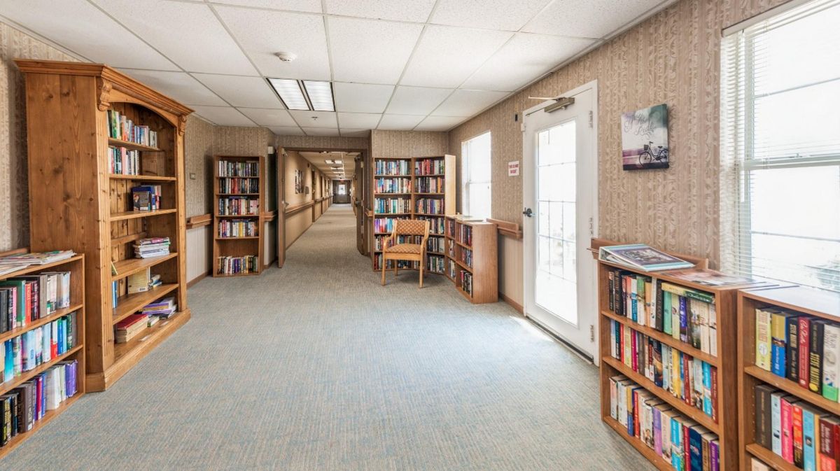 A quiet library hallway lined with bookshelves and a small reading area by a doorway.