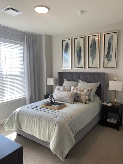 A modern bedroom with elegant decor and artwork, featuring a neatly made bed with natural light streaming in through the window.