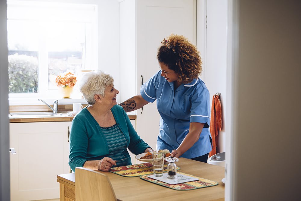A caregiver assists an elderly woman in a home setting.