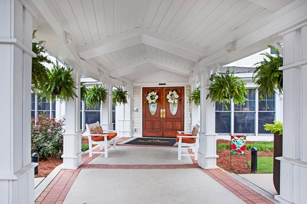 A welcoming porch with hanging plants and decorated double front doors.