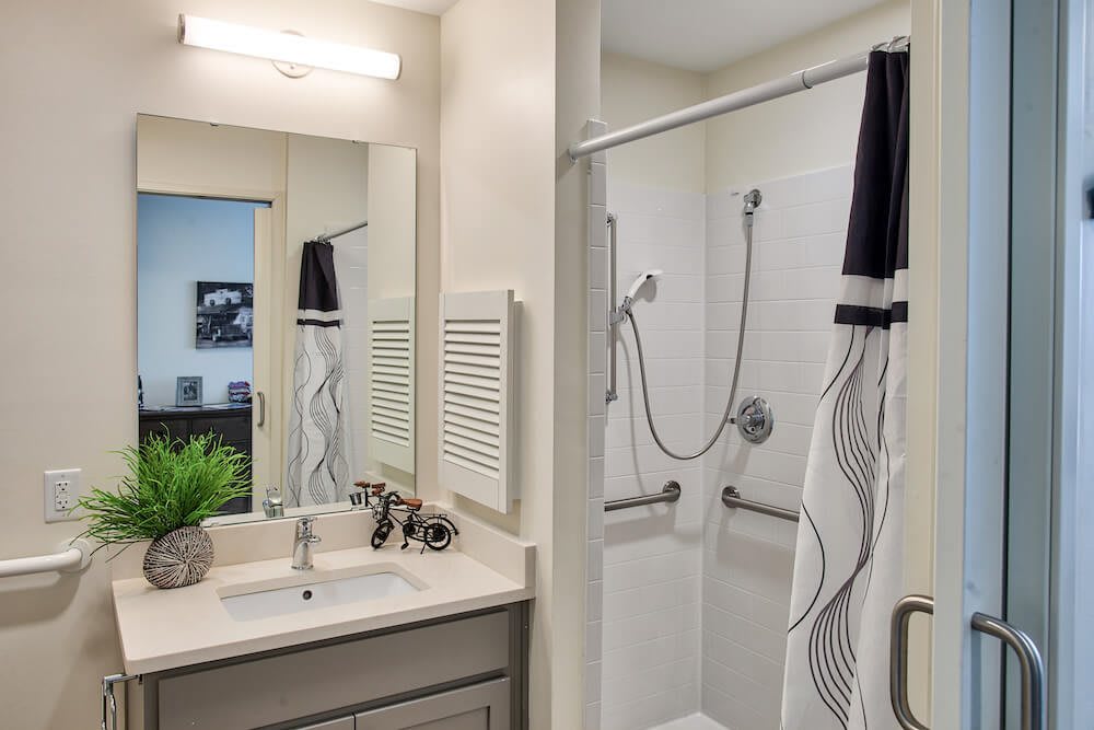 A modern bathroom with a sink and mirror next to a shower area with patterned curtains.
