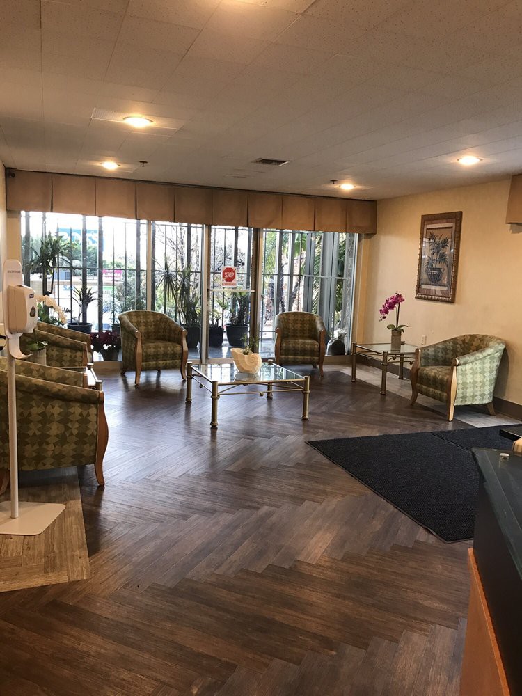 A cozy waiting area with comfortable seating, tables, and plants by large windows.