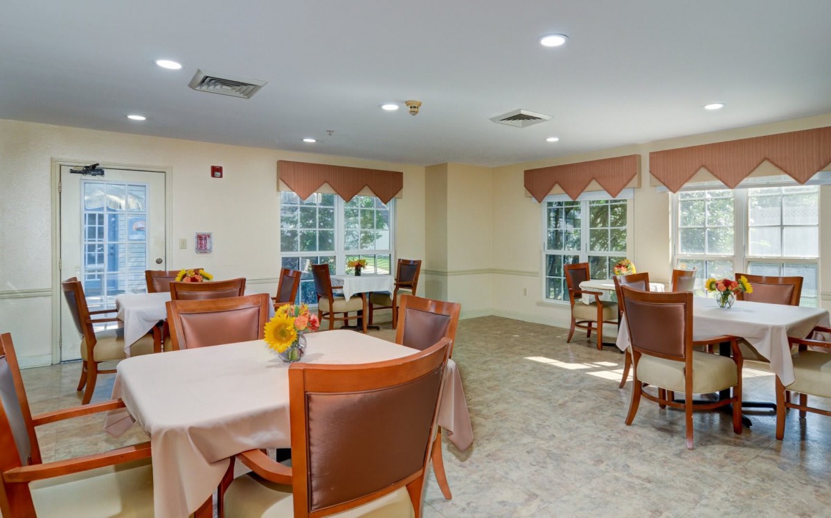 A well-lit dining area with tables and chairs, decorated with sunflowers near large windows.