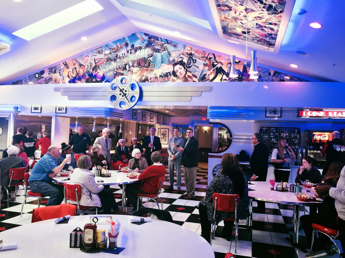 A bustling retro diner with a colorful decor and a checkerboard floor, filled with people enjoying their meals.