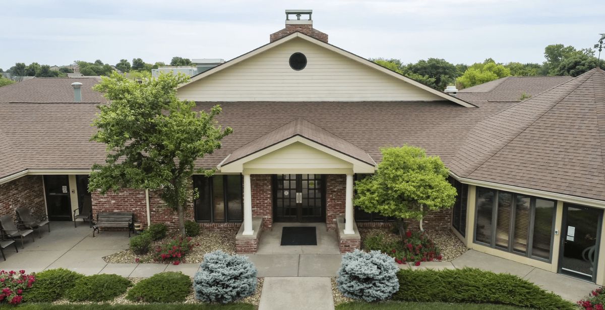 Front view of a brick building with an entrance flanked by pillars and surrounded by landscaped greenery.