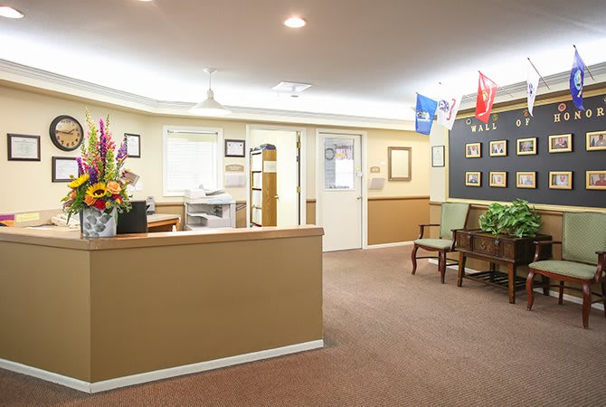 A well-lit reception area with a desk, chairs, and flags on display.
