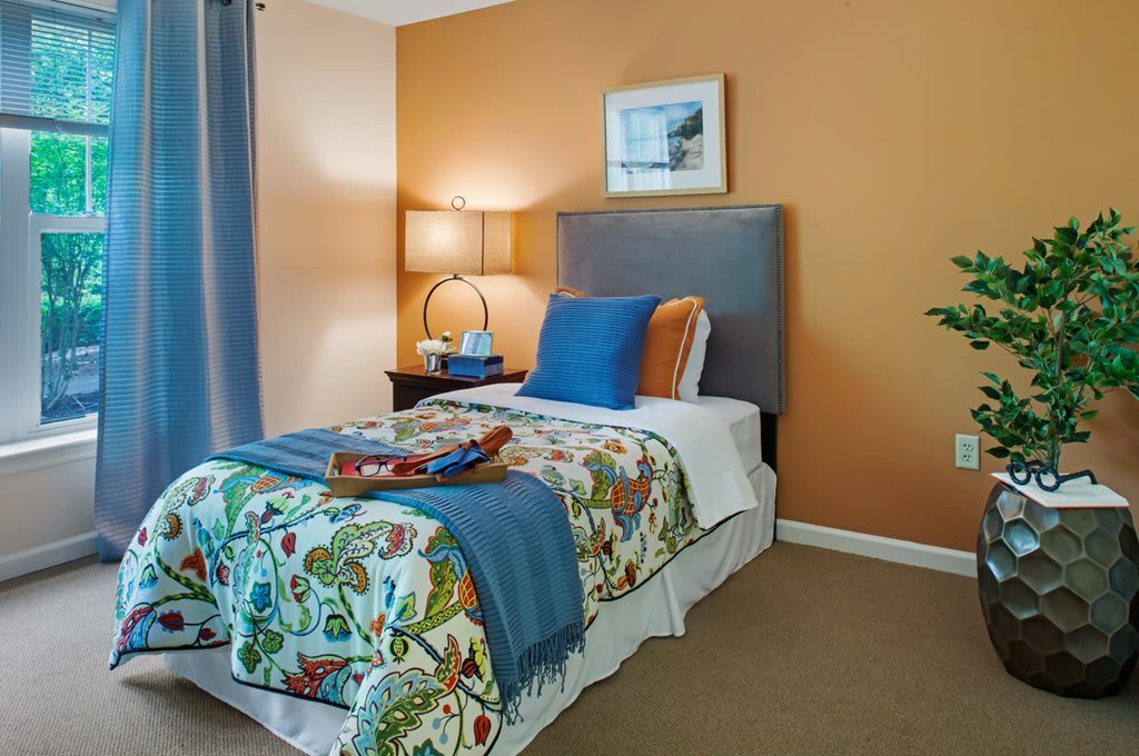 A cozy bedroom with a single bed featuring colorful bedding, an orange accent wall, and a stylish lamp on the side table.