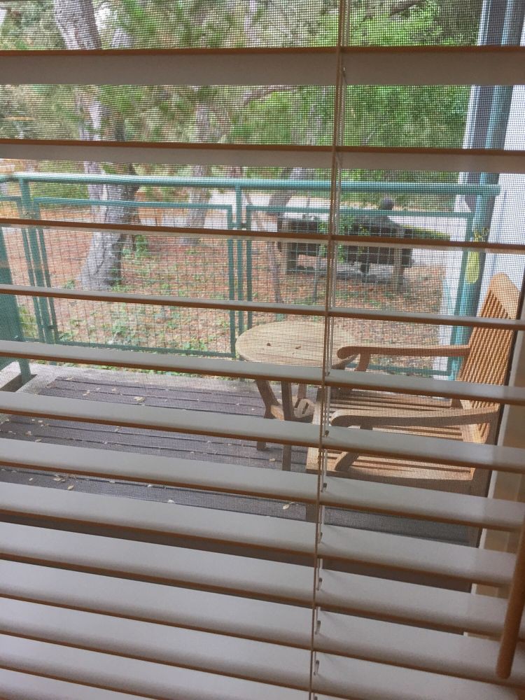 A view of outdoor furniture through window blinds, featuring a wooden deck with chairs and a table.