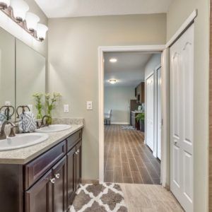 A modern bathroom with a double sink vanity and a view into an adjoining room.