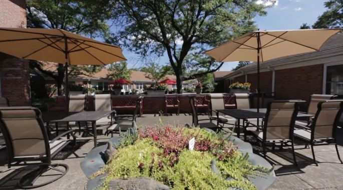An inviting outdoor patio area with tables, chairs, and umbrellas surrounded by lush greenery on a sunny day.