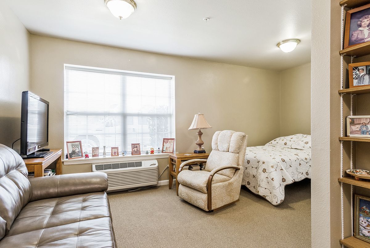 A cozy bedroom with a bed, armchair, and a window providing natural light.