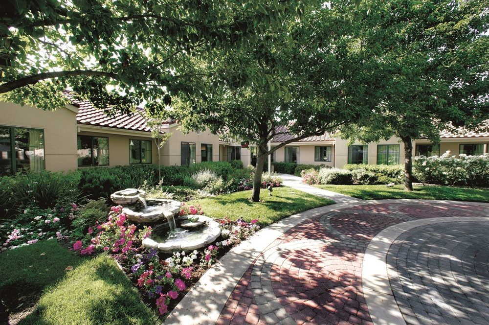 A serene garden landscape with a pathway, surrounded by flowers and trees.