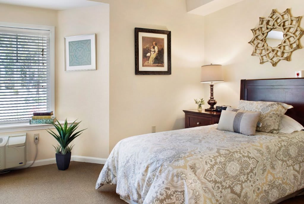 A cozy bedroom with elegant decor, featuring a large bed, artwork on the walls, and a bedside lamp.