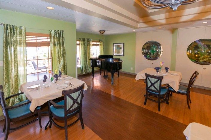 A cozy dining room with a grand piano, featuring elegant tables and chairs on a wooden floor.