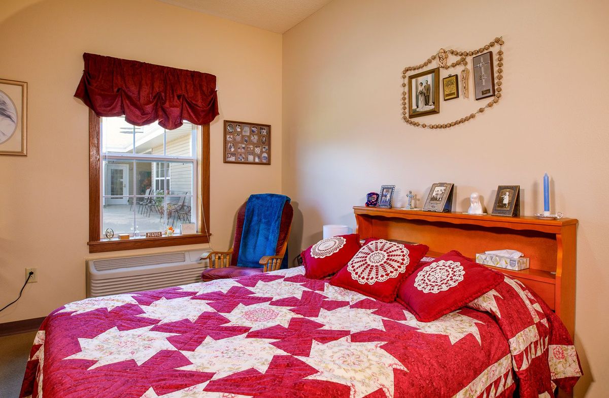 A cozy bedroom featuring a bed with a red and white patterned quilt, decorated walls, and a large window.