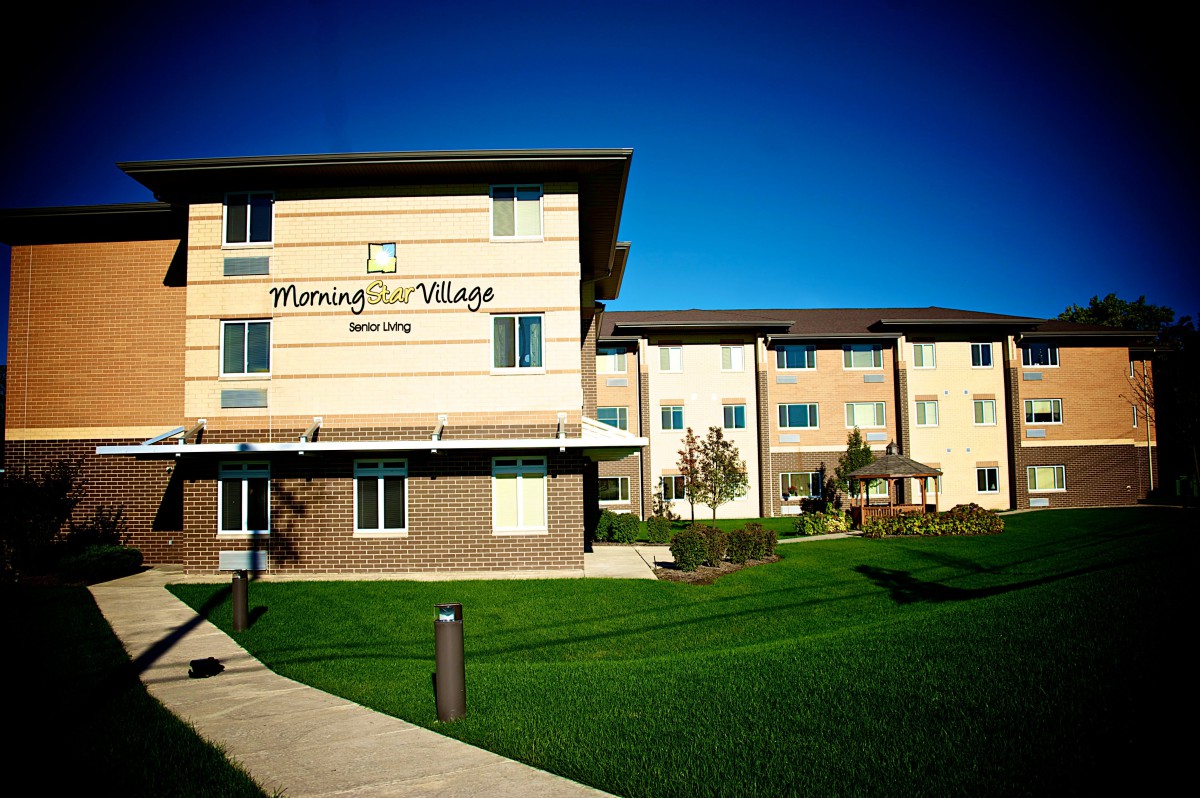 A modern apartment building with a well-maintained lawn and clear blue sky.