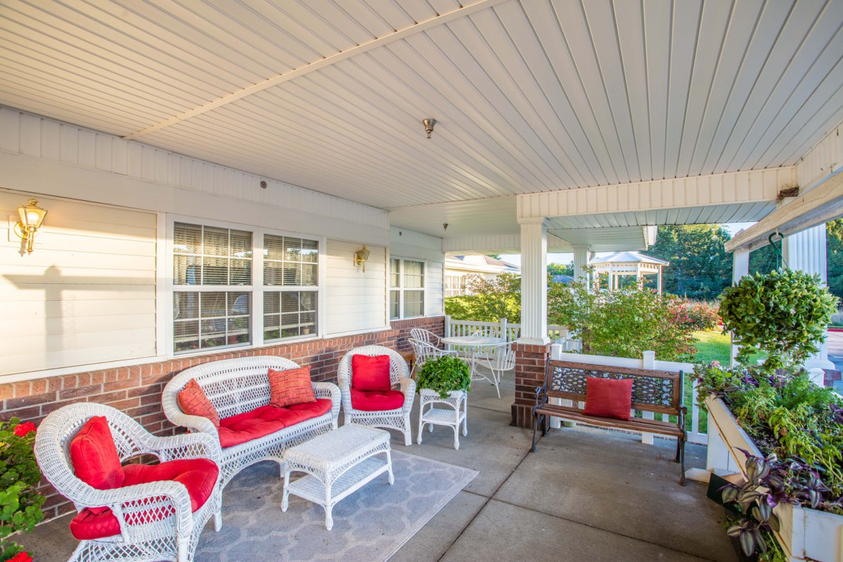 A cozy porch with wicker furniture and red cushions, perfect for relaxing outdoors.