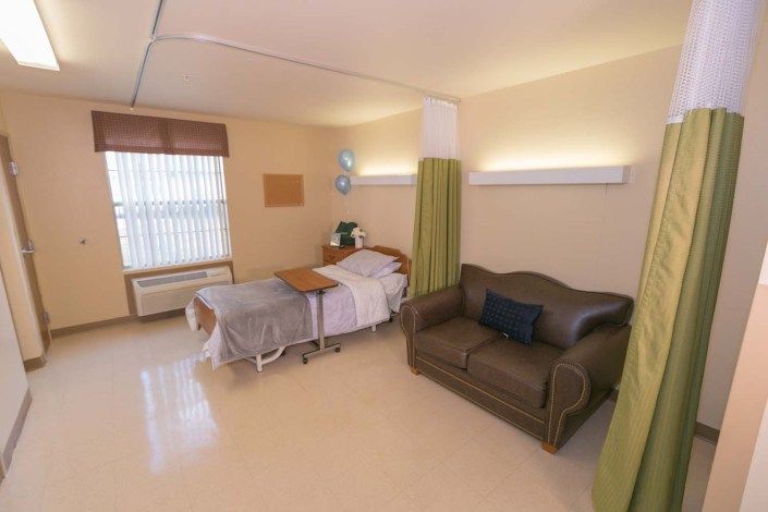 A clean and organized hospital room featuring a bed, a couch, and light-colored curtains.