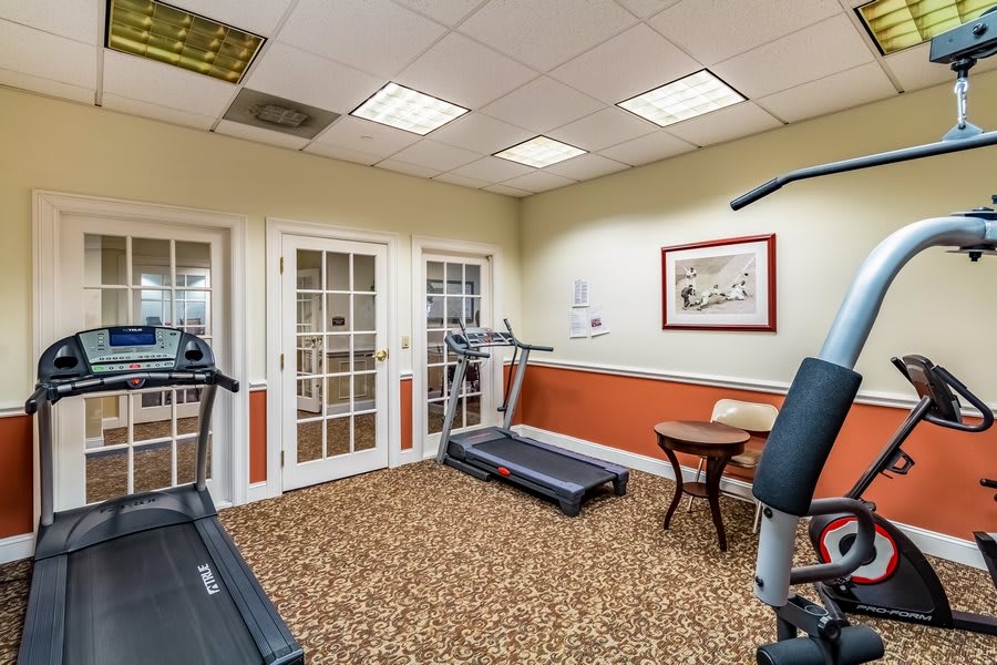 A small, carpeted fitness room featuring exercise equipment including treadmills and weight machines.