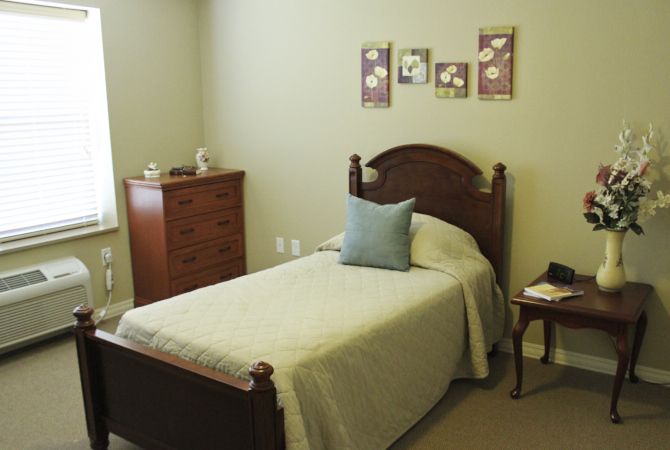 A cozy bedroom with a single bed, dresser, and nightstand, featuring simple decor.