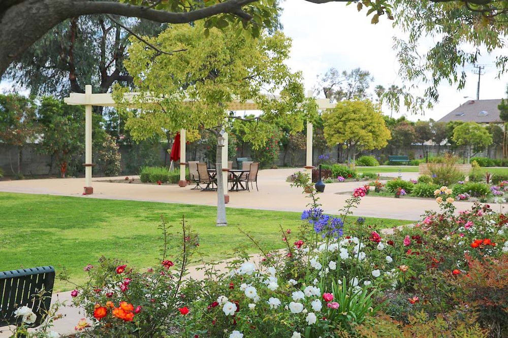 A beautifully landscaped garden with colorful flowers and a patio seating area surrounded by trees.