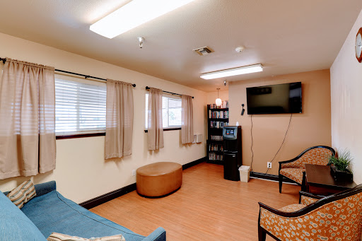 A cozy waiting area featuring comfortable seating, a television, and natural light from the windows.