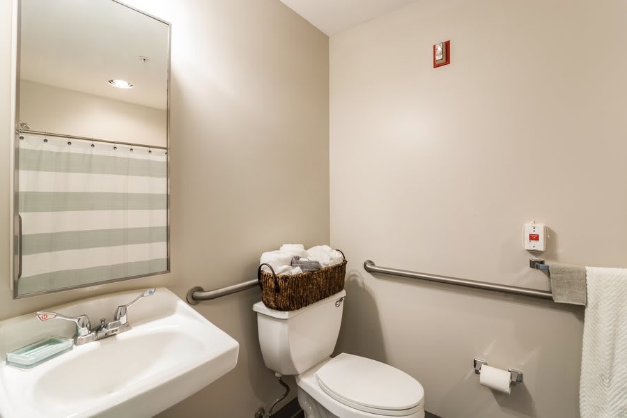 A clean, accessible bathroom with a sink, toilet, and mirror.