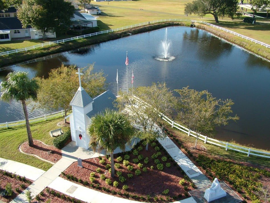 A scenic aerial view of a park featuring a pond with a central fountain, surrounded by pathways and lush greenery.