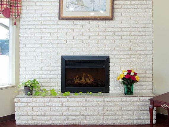 A cozy room with a brick fireplace, adorned with plants and flowers.