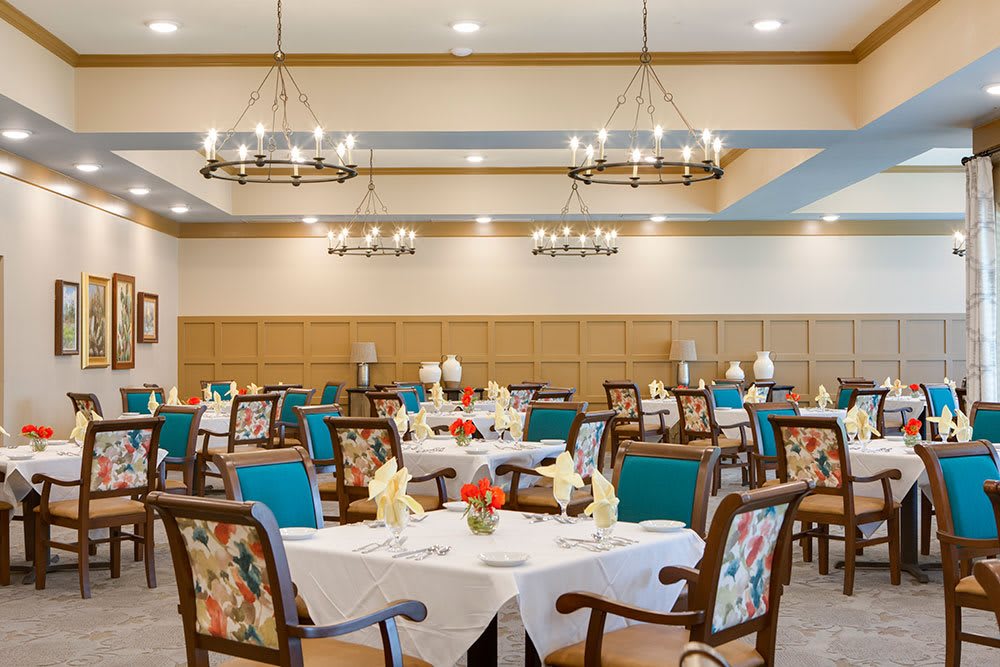 A well-decorated dining room with elegantly set tables and chairs, featuring warm lighting and floral decor.