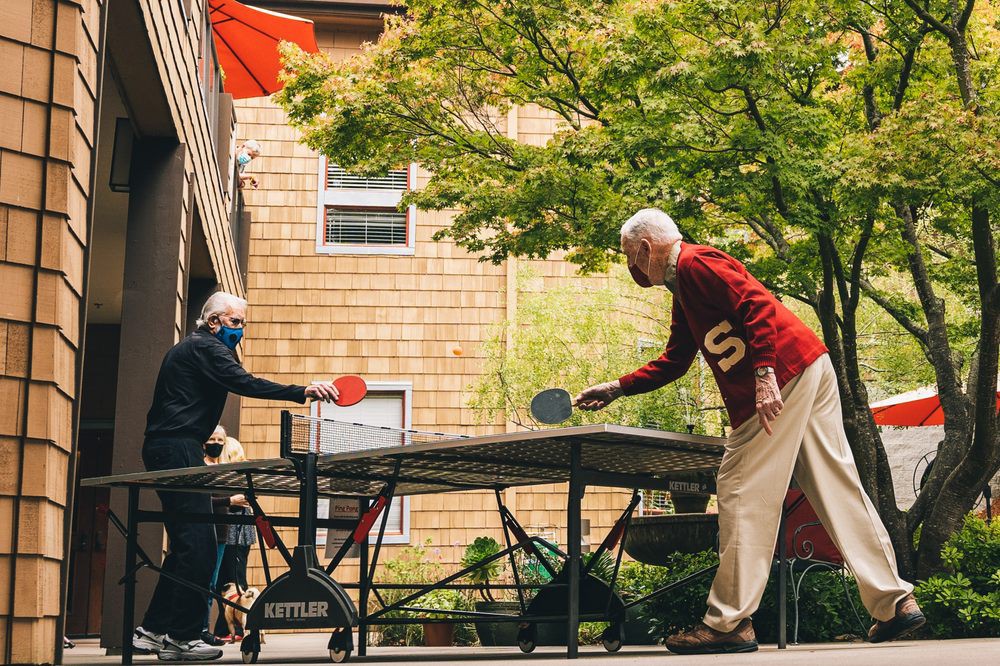 Two elderly individuals enjoying a game of table tennis outdoors.