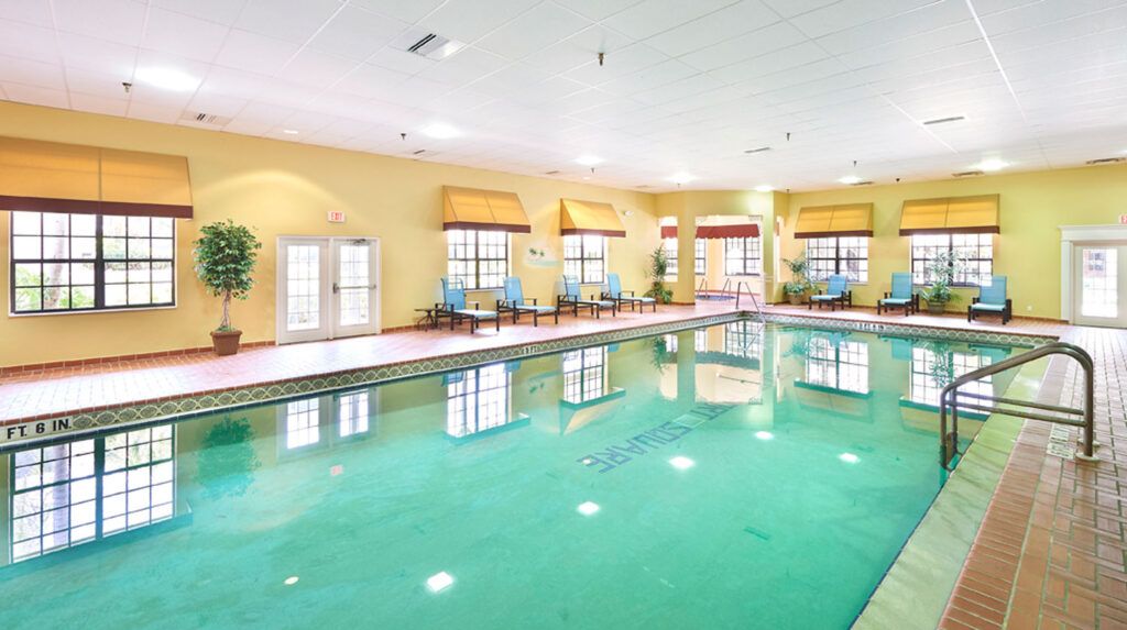 A spacious indoor swimming pool surrounded by chairs and large windows.