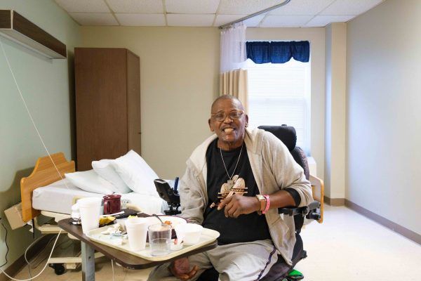 A patient in a wheelchair smiling in a hospital room.