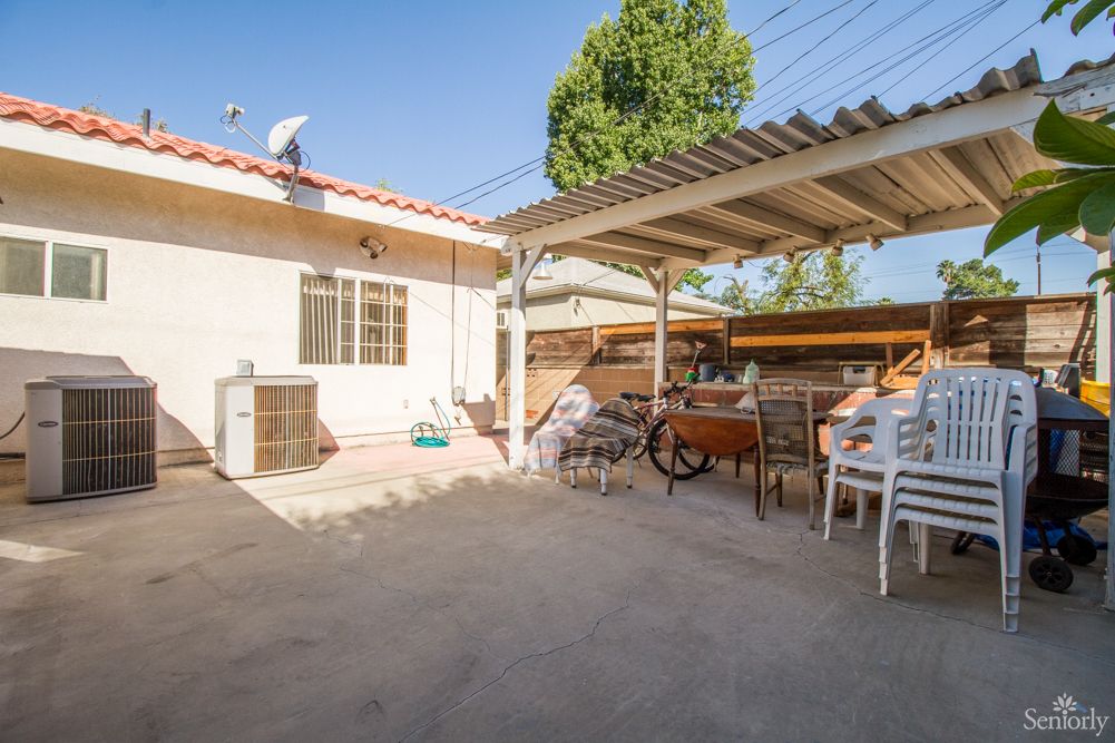 A sunny backyard patio with outdoor seating and a bicycle under a shade structure.