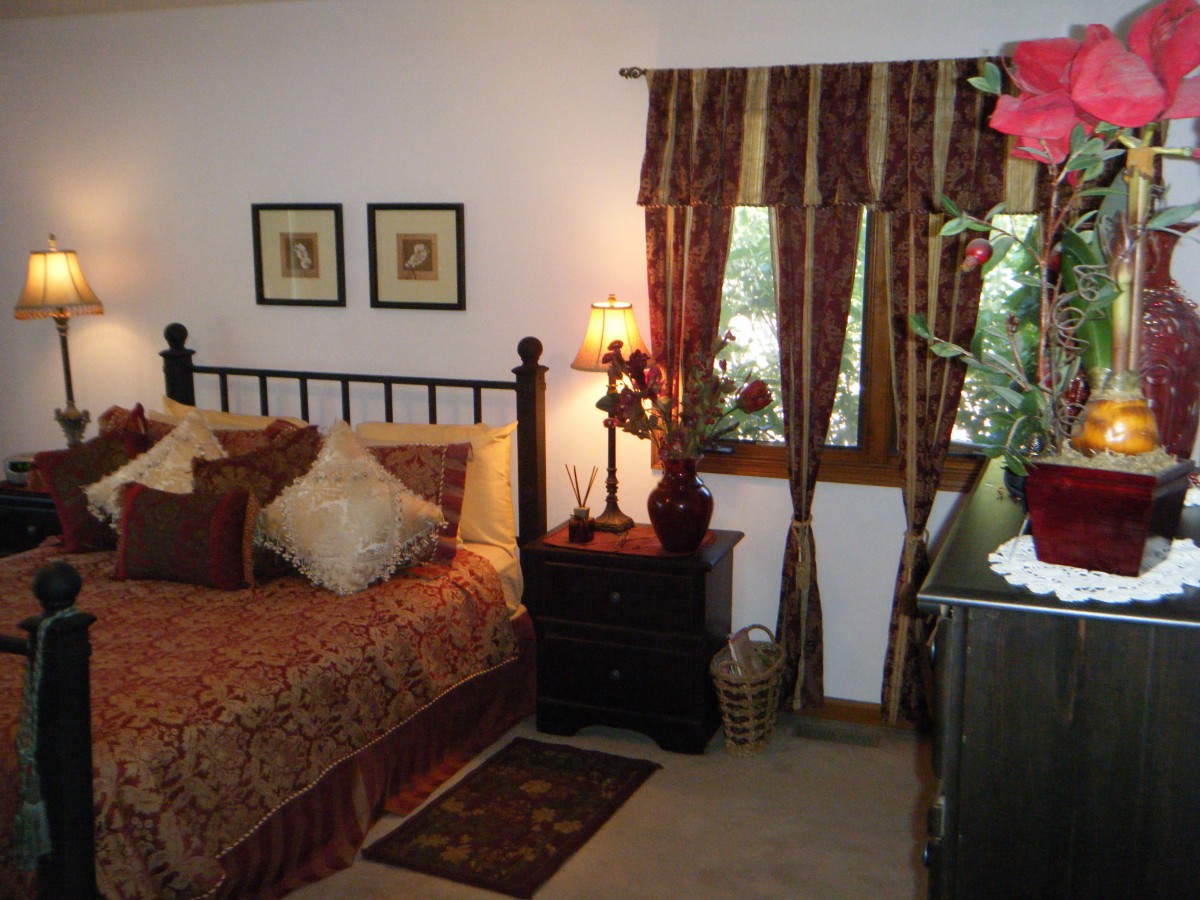 A cozy bedroom with elegant decor, featuring a bed, nightstand with a lamp, and a window with patterned curtains.