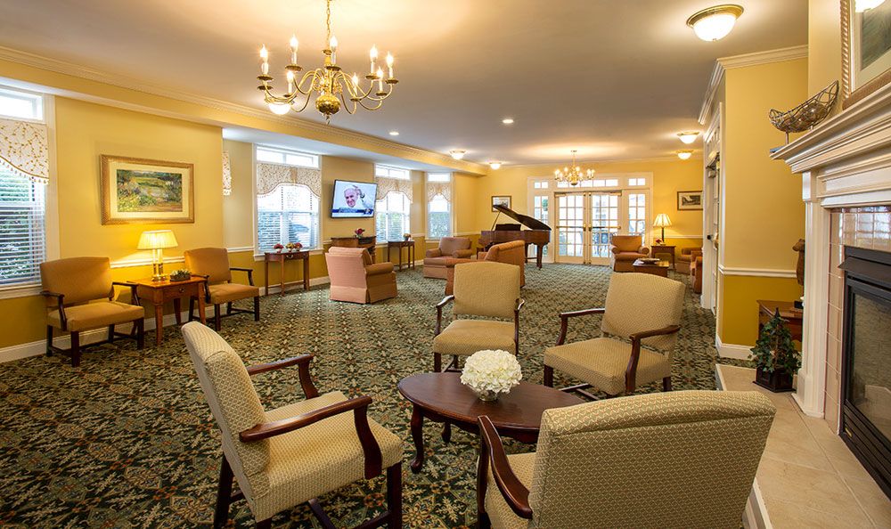 A spacious and elegantly furnished living room with comfortable seating, a grand piano, and a chandelier.