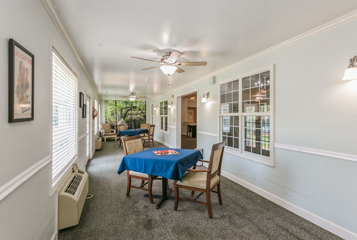 A cozy interior dining area with tables and chairs, featuring large windows and a ceiling fan.