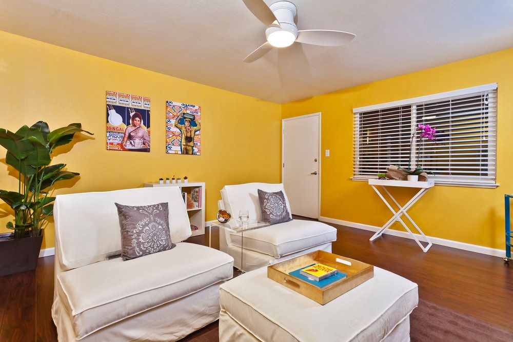 A cozy living room with yellow walls and white furniture, featuring modern decor and a ceiling fan.