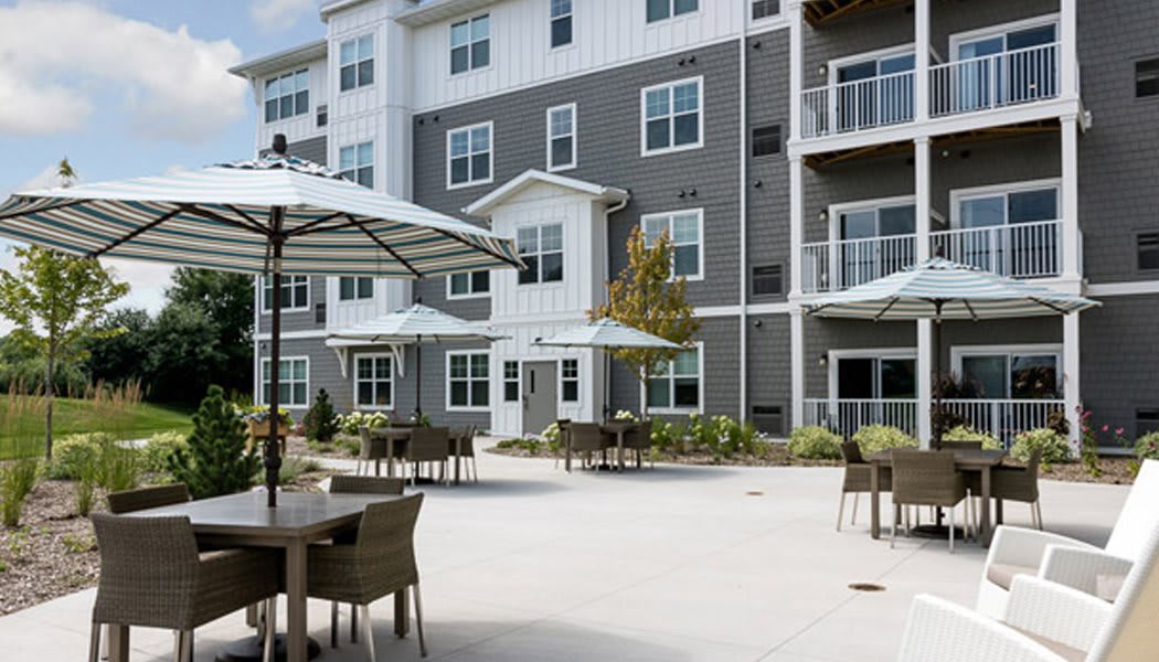 A modern apartment building with an outdoor patio featuring tables, chairs, and umbrellas.