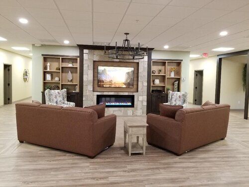 A cozy living room setup with sofas facing a fireplace, flanked by bookshelves and illuminated by a chandelier.