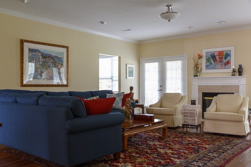 A cozy living room with a blue sofa, armchair, and a coffee table on a patterned rug, featuring a fireplace and artwork on the walls.