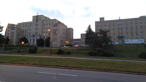 A view of several buildings set against a cloudy sky, with green landscaping in the foreground.